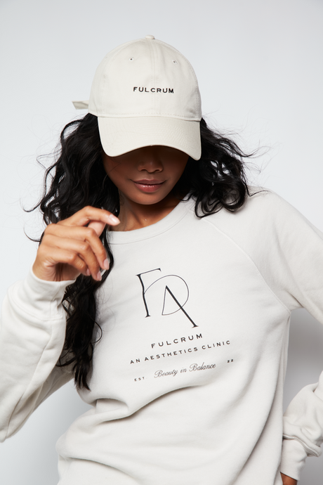 Model wearing Fulcrum crewneck and matching cap in neutral tones, looking down with relaxed pose.