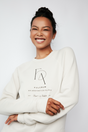 Model wearing a cream Fulcrum crewneck sweater with minimalist black logo, smiling softly.