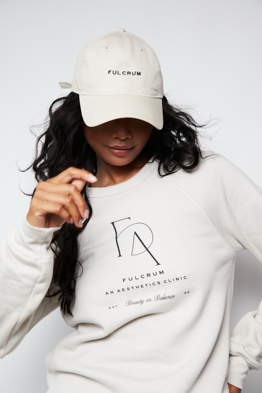 Model wearing Fulcrum crewneck and matching cap in neutral tones, looking down with relaxed pose.