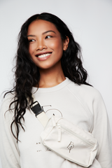 Model wearing the Fulcrum Fanny Pack in cream nylon with embroidered logo, styled crossbody over a Fulcrum crewneck sweatshirt.